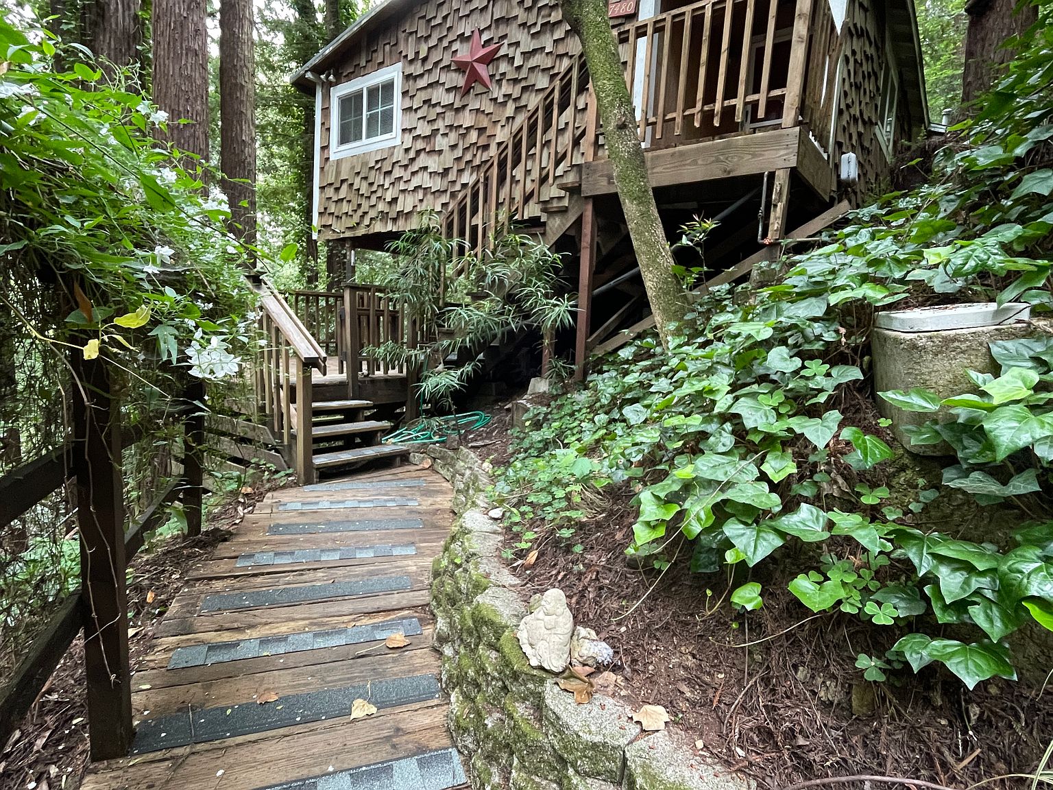 A shingled cabin among redwoods with a wooden walkway